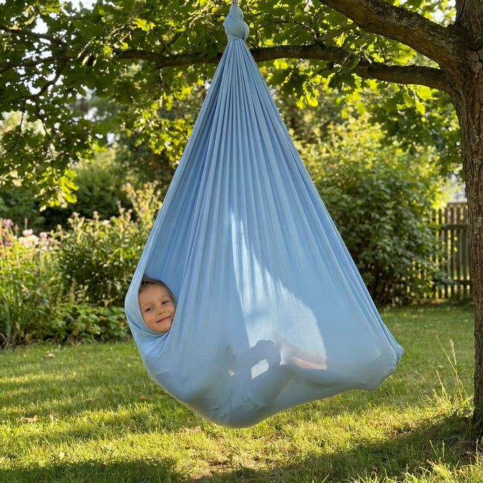 Kind schaukelt in der blauen Therapieschaukel am Baum im Garten