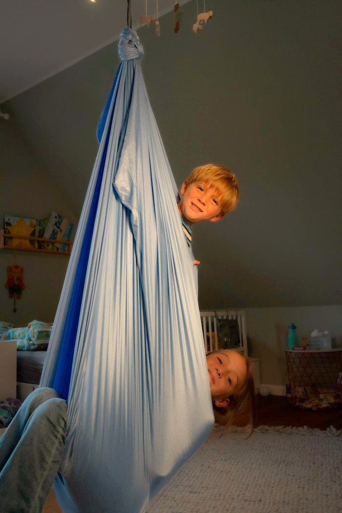 Zwei Kinder schauen aus der blauen Therapieschaukel im Kinderzimmer
